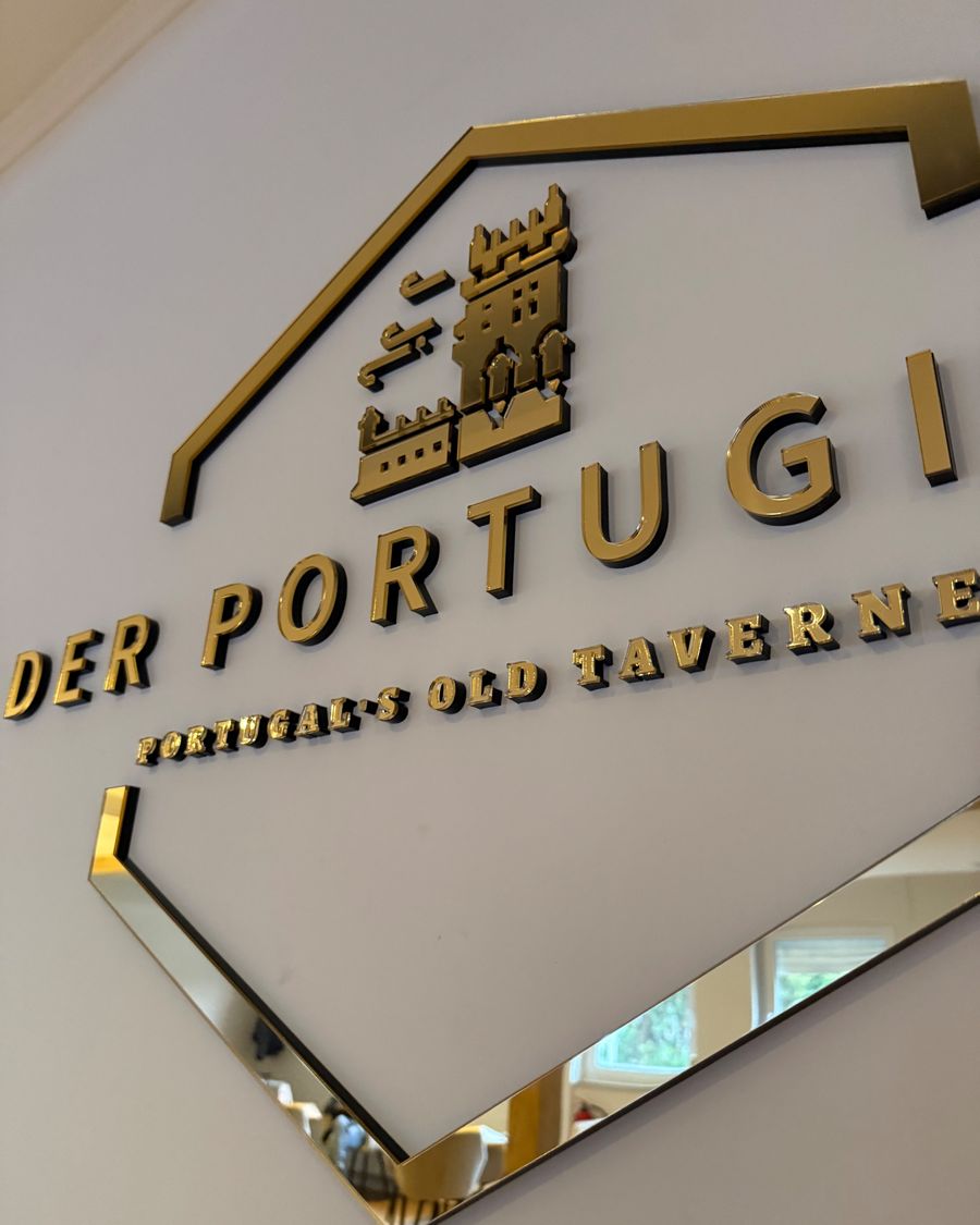 Angeschnittene Nahaufnahme des goldenen 3D-Wandlogos "DER PORTUGIESE" mit verspiegeltem Chevron im Innenbereich