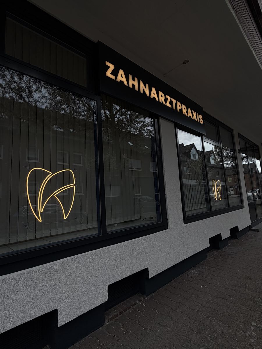 Außenfassade der Zahnarztpraxis Roja Balhas in Selm mit beleuchtetem Schriftzug „ZAHNARZTPRAXIS" in warmweißen Vollacryl-Buchstaben und den warmweißen LED-Neon-Logos an den Fensterscheiben