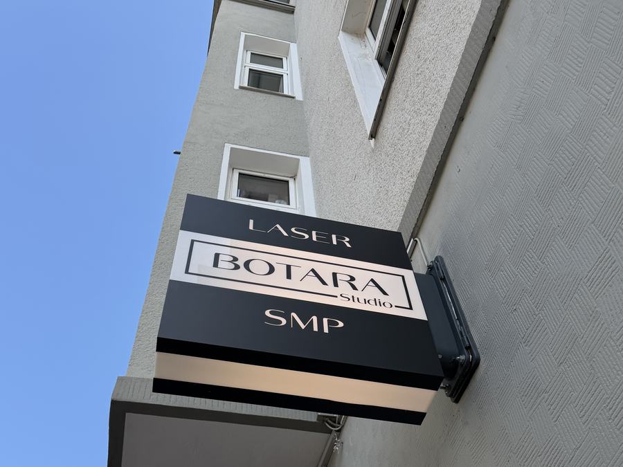 Beidseitiges Auslegerschild LASER BOTARA Studio SMP von unten fotografiert, blauer Himmel