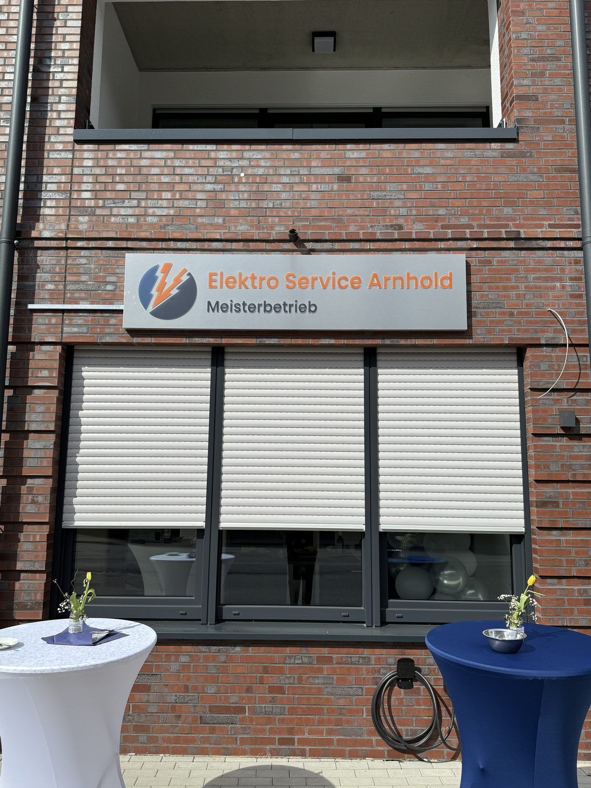 Frontalansicht des Wandschildes von Elektro Service Arnhold mit orangefarbenen 3D-Buchstaben, Zusatz Meisterbetrieb und Blitz-Logo, reale Umsetzung von Visuellewand