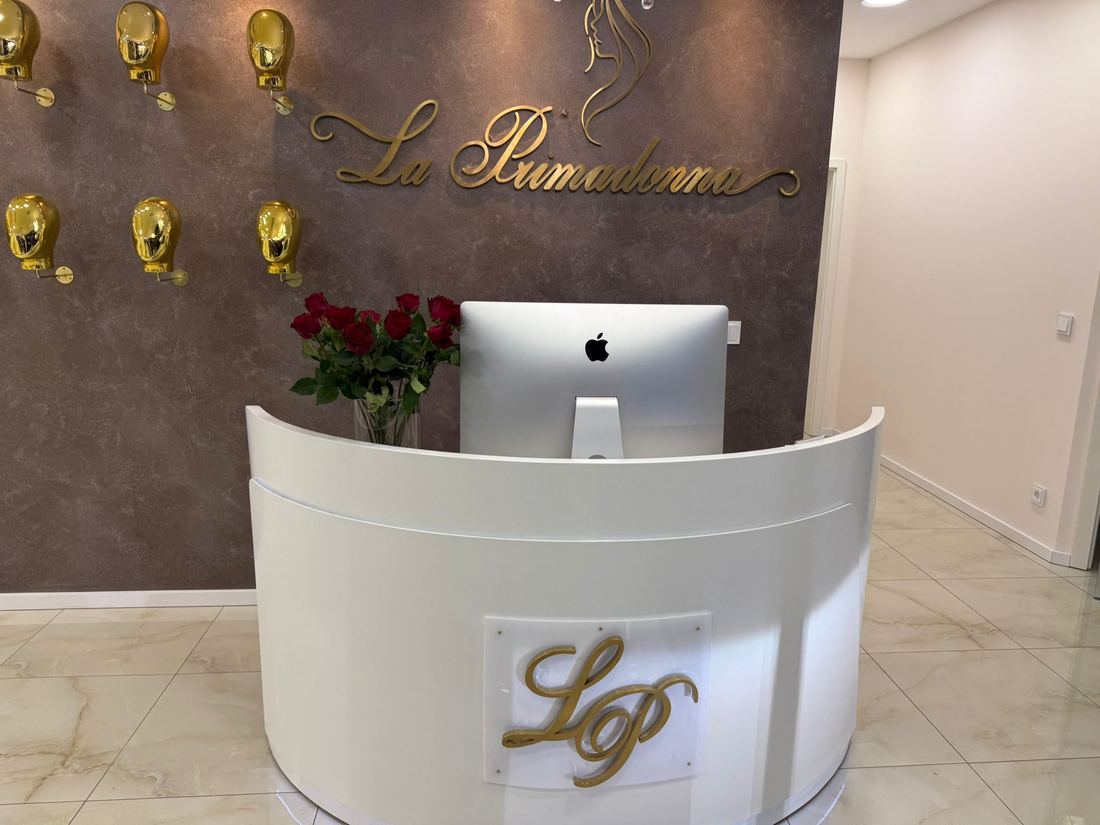 Empfangstresen von La Primadonna mit goldenem LP-Monogramm, Rosenstrauß und dem Wandlogo im Hintergrund