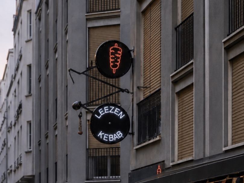 Fahrrad-förmiger Auslegerschild von Leezen Kebab mit rotem Döner-Symbol und weißem LED-Neon-Schriftzug
