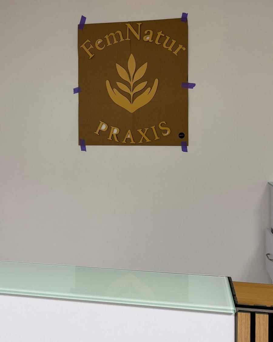 Fertiges 3D-Wandlogo FemNatur Praxis über dem Empfangstresen mit Glasablagen