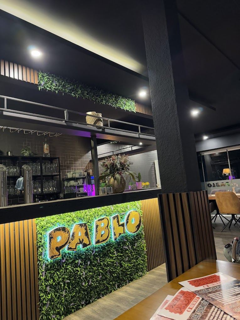 Gastraum der Pizzeria Pablo mit Blick auf die Theke und das beleuchtete PABLO-Logo im Hintergrund