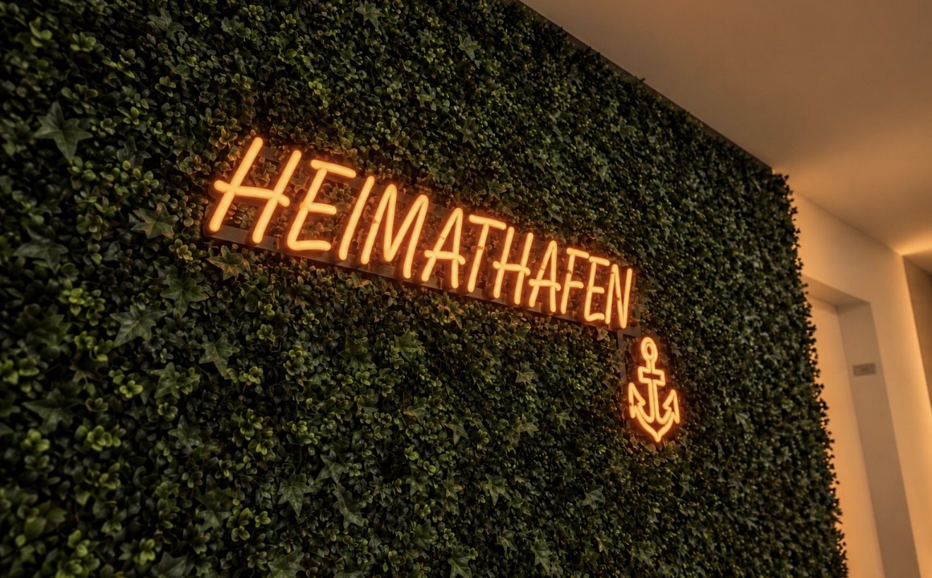 LED-Neon-Schild mit Schriftzug HEIMATHAFEN und Anker in Orange auf der Kunstpflanzenwand im Flur der Ärzteversorgung Westfalen-Lippe in Münster, gefertigt von Visuellewand