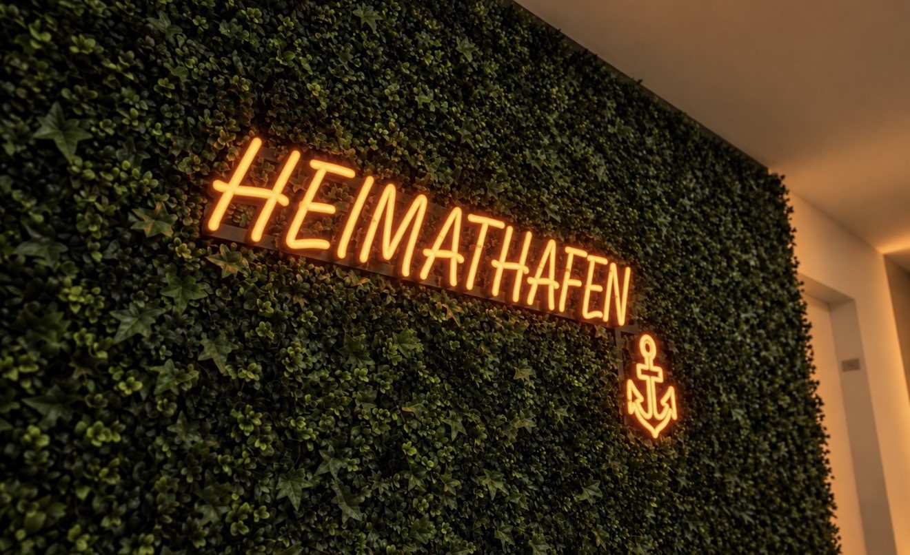 LED-Neon-Schild mit Schriftzug HEIMATHAFEN und Anker in Orange auf der Kunstpflanzenwand im Flur der Ärzteversorgung Westfalen-Lippe in Münster, gefertigt von Visuellewand
