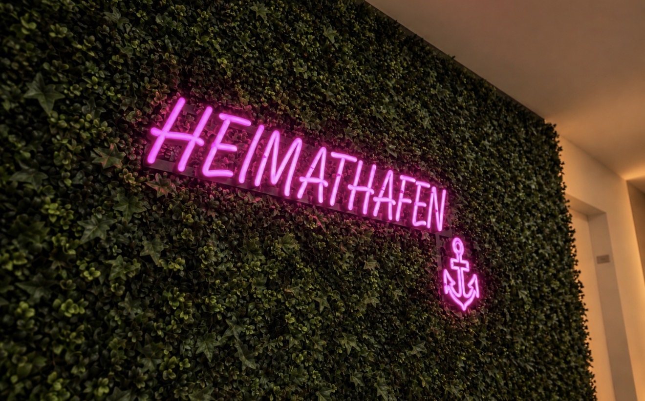 LED-Neon-Schild mit Schriftzug HEIMATHAFEN und Anker in Pink auf der Kunstpflanzenwand im Flur der Ärzteversorgung Westfalen-Lippe in Münster, gefertigt von Visuellewand