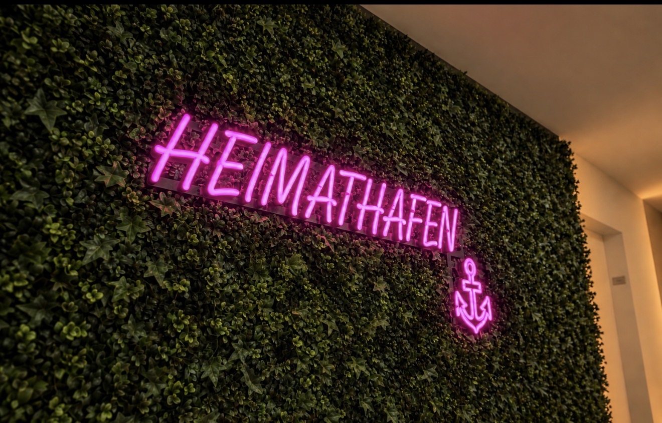 LED-Neon-Schild mit Schriftzug HEIMATHAFEN und Anker in Pink auf der Kunstpflanzenwand im Flur der Ärzteversorgung Westfalen-Lippe in Münster, gefertigt von Visuellewand