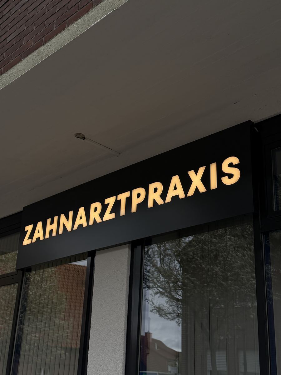 Nahansicht der Leuchtreklame „ZAHNARZTPRAXIS" in warmweiß leuchtenden, 10 mm dekupierten Vollacryl-Buchstaben auf dem anthrazitfarbenen Alu-Dibond-Kasten