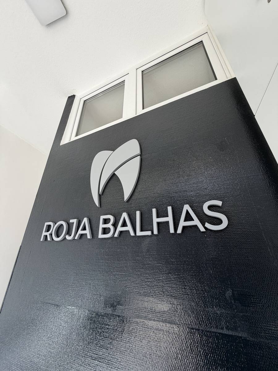 Nahansicht des 3D-Wandlogos „ROJA BALHAS" auf der anthrazitfarbenen Wand im Eingangsbereich, aus einem seitlichen Blickwinkel fotografiert
