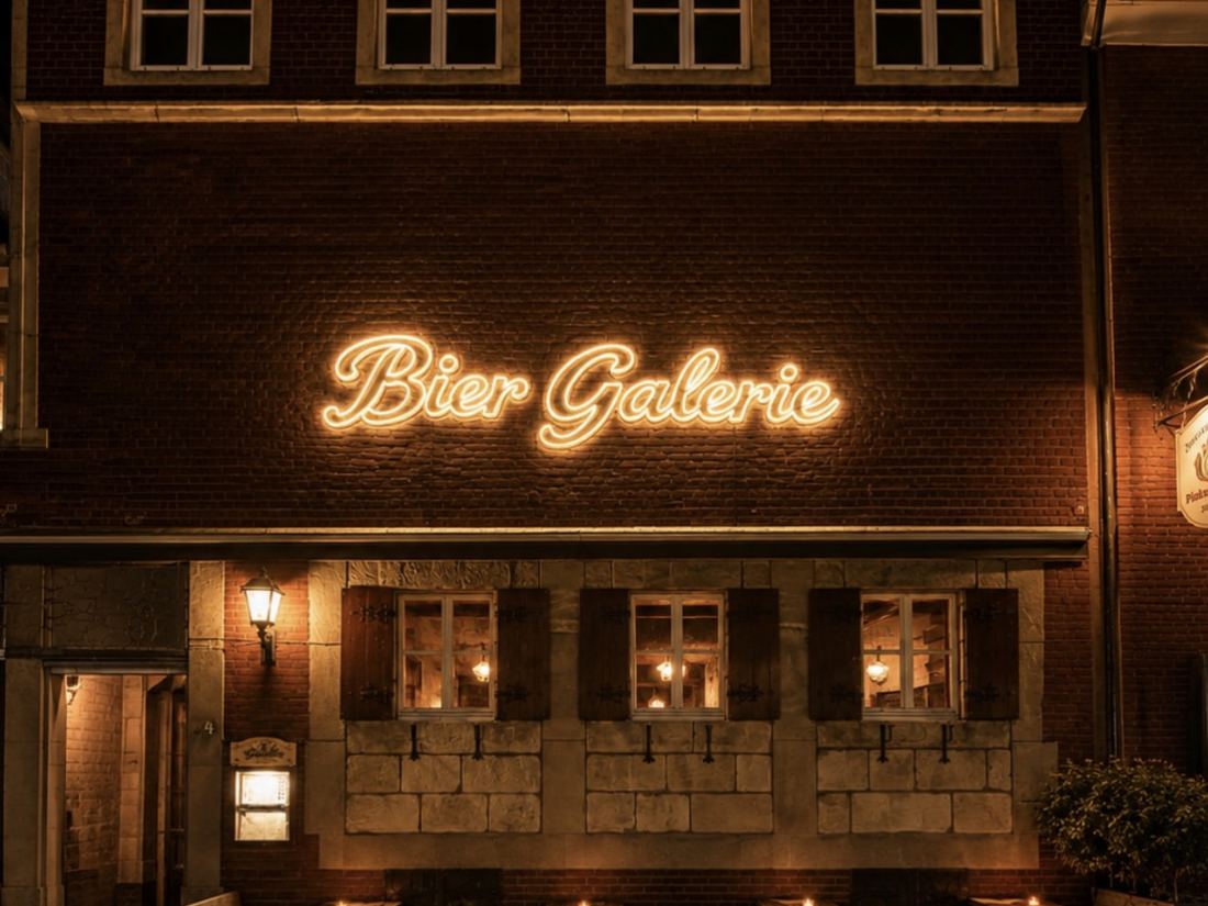 Nahansicht des warmweißen LED-Neon-Schriftzugs „Bier Galerie“ mit Außenterrasse im Vordergrund, Münster