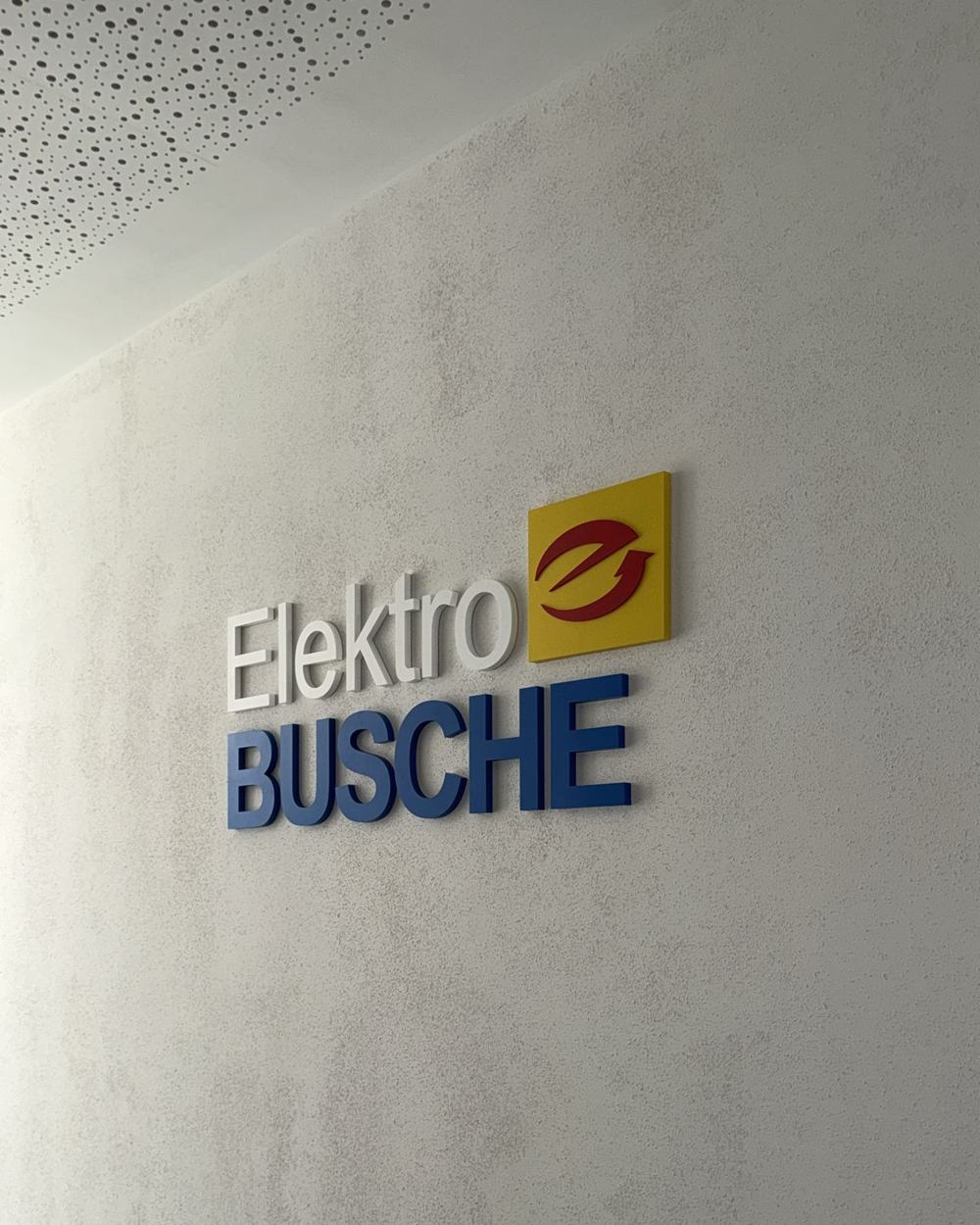 Nahaufnahme des 3D-Wandlogos Elektro Busche, Schriftzug und Firmensymbol in Firmenfarben lackiert