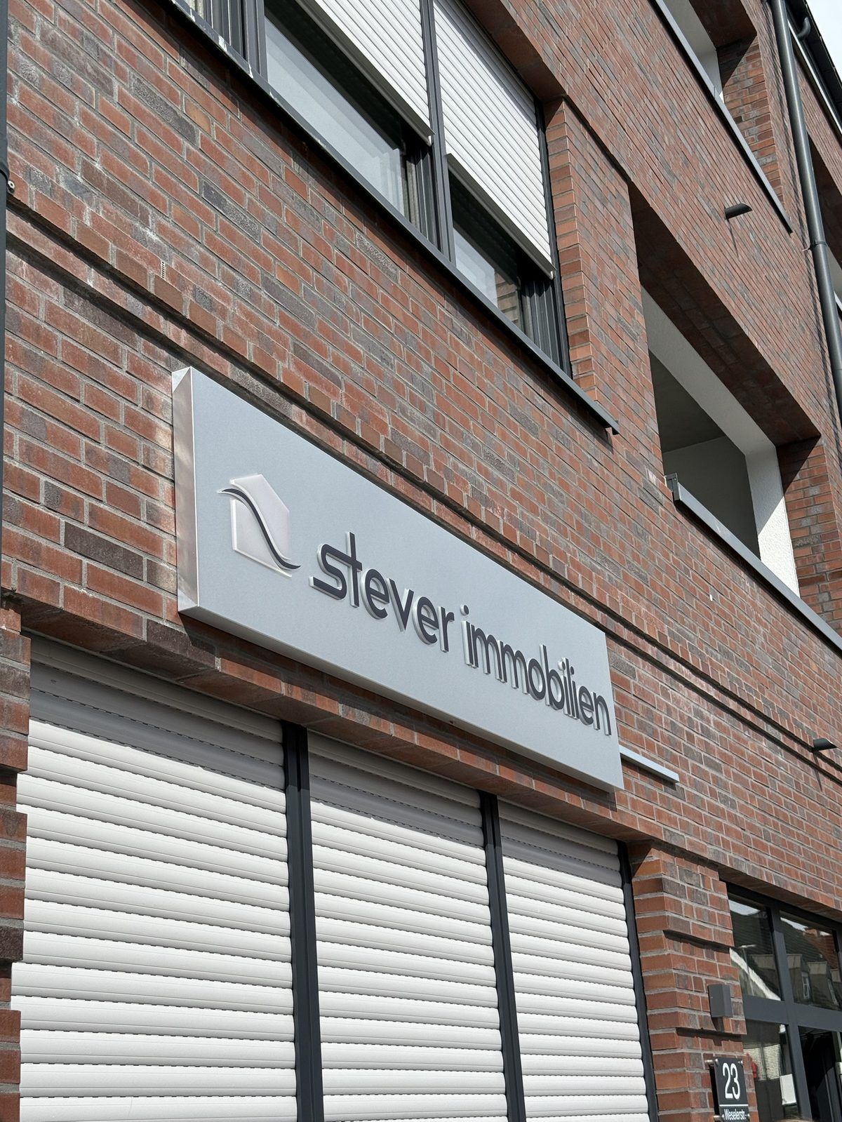 Schrägansicht des Stever-Immobilien-Schildes mit plastisch aufgesetzten 3D-Buchstaben und Logo, reale Umsetzung von Visuellewand
