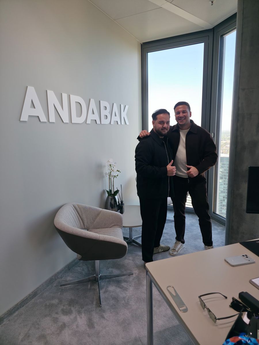 Zwei Personen zeigen den Daumen hoch vor dem 3D-Wandlogo „ANDABAK" im Büro im Hochhaus „The Four", Frankfurt am Main
