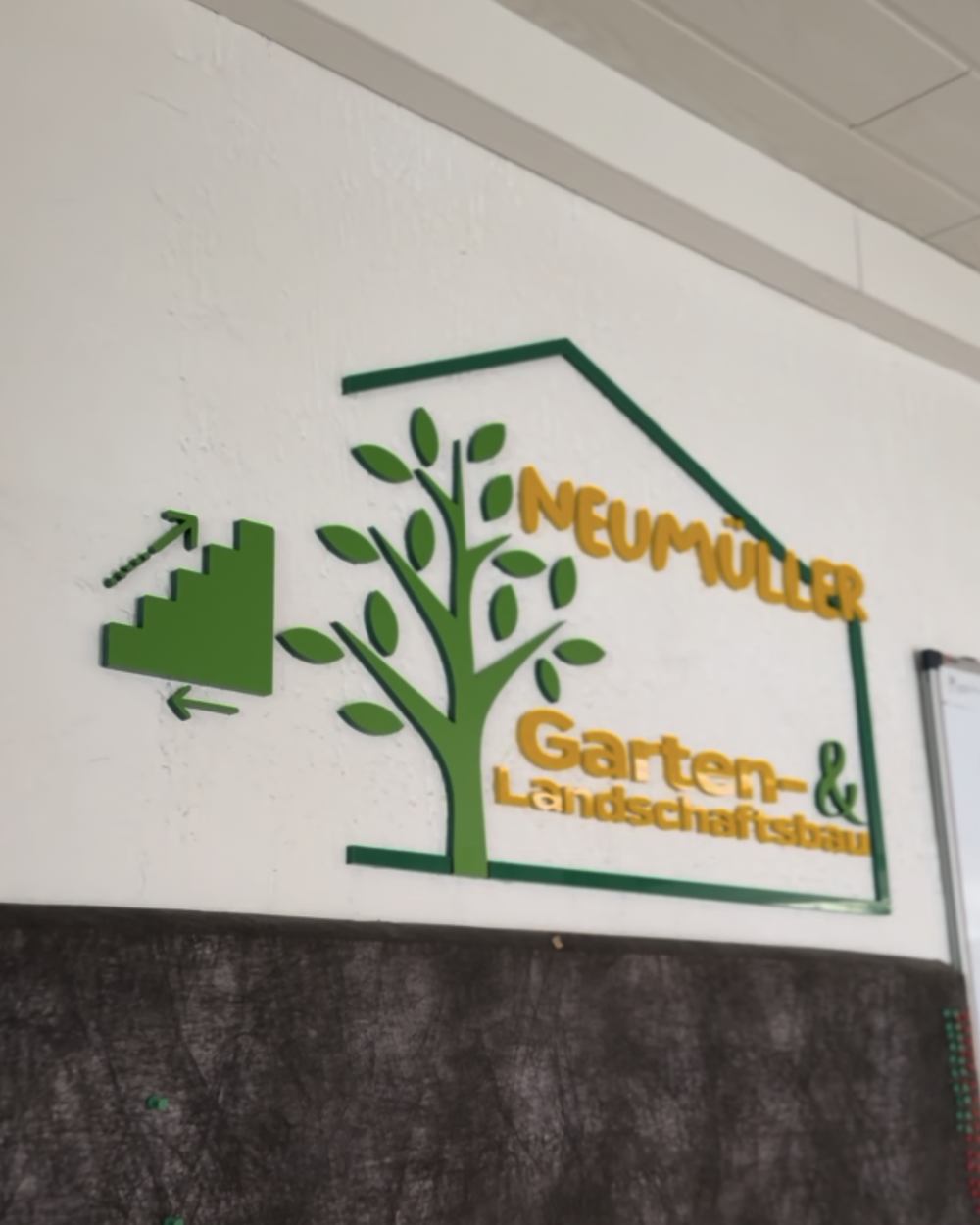 Zweites 3D-Wandlogo von GALA Bau Neumüller mit Wegweiser-Pfeil und Treppen-Symbol als Hinweis zum Büro